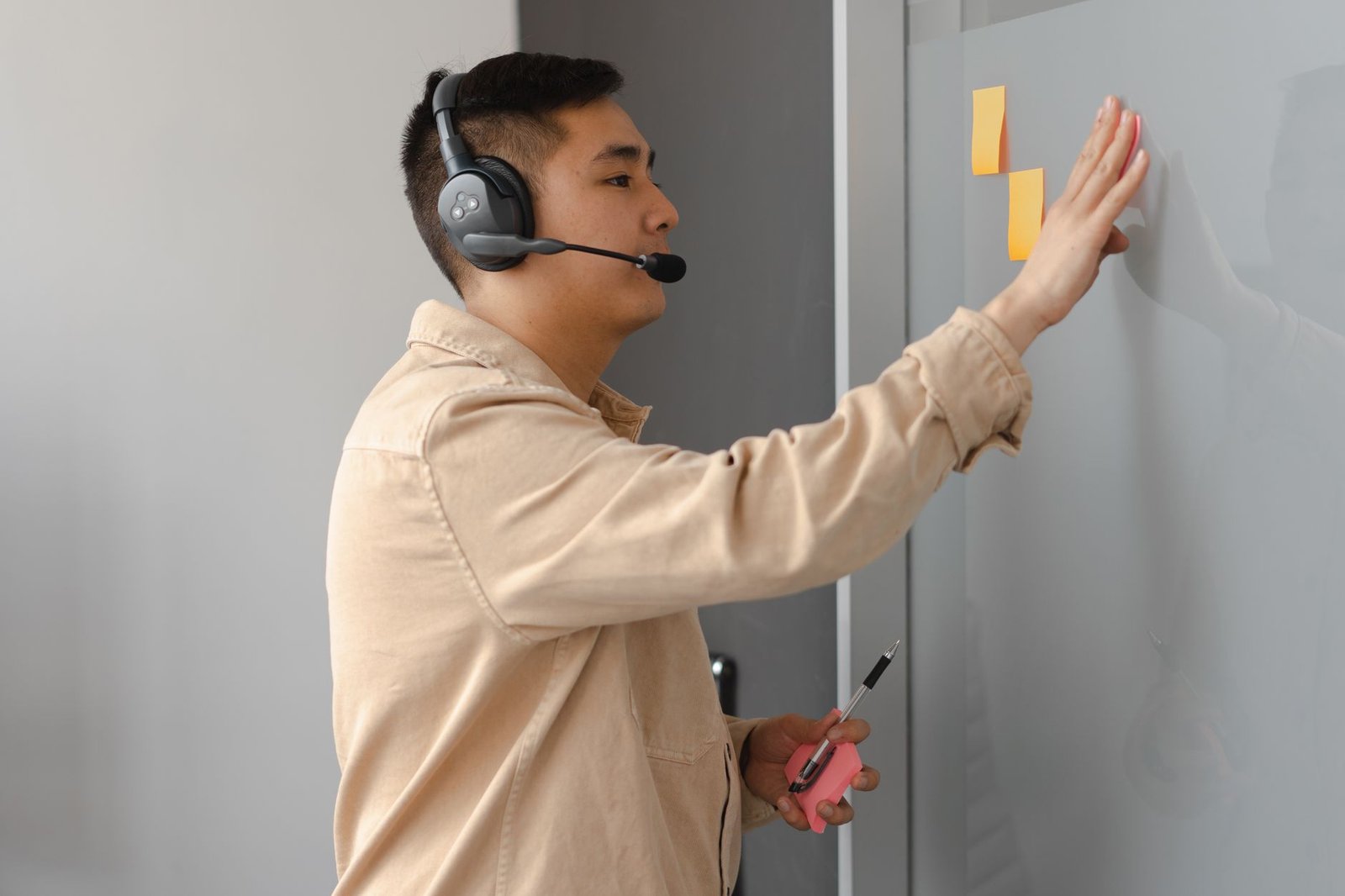 Asian male customer service agent using sticky notes and headset in an office setting.