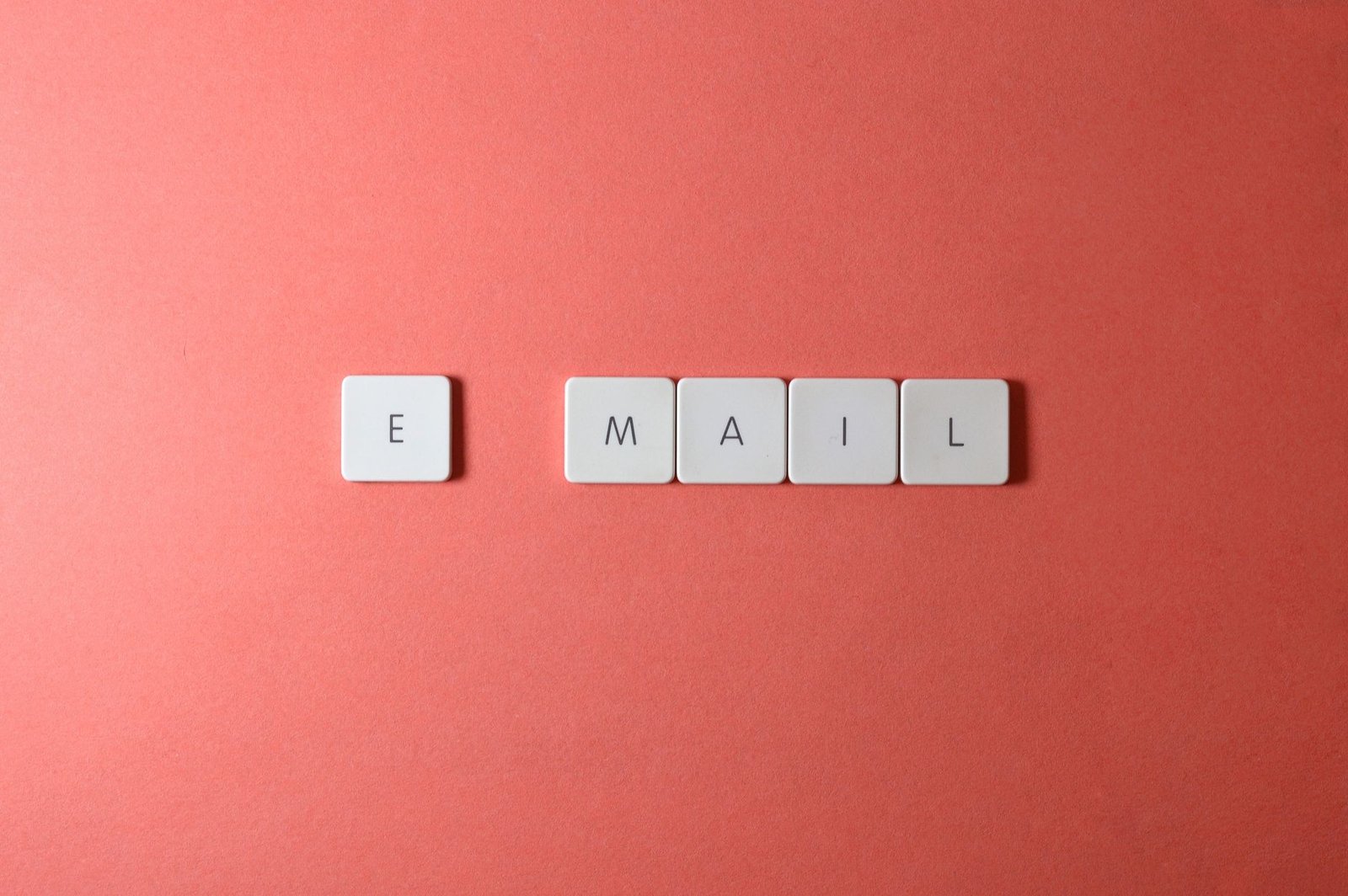 Flat lay of keyboard letter tiles spelling 'email' on coral backdrop.