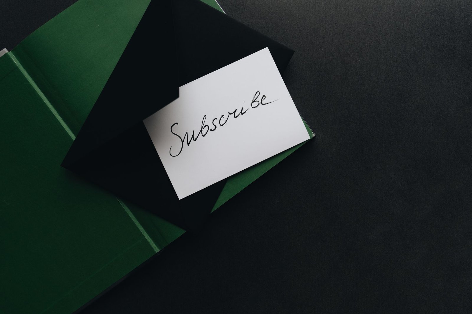 A minimalist image of a 'Subscribe' card in a green envelope on a dark background.